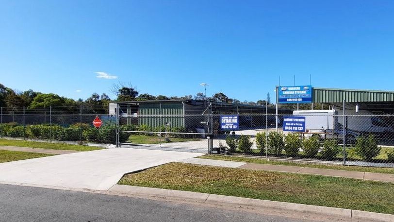 The street frontage of Urangan Caravan Storage on Southern Cross Circuit, with the fence line, the entry gate and clear Queensland sky.