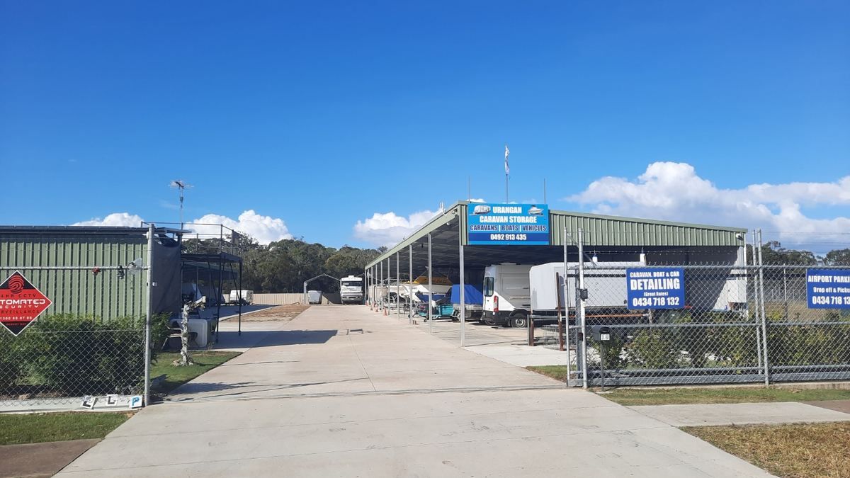 The open-air hardstand at Urangan Caravan Storage, a wide concrete driveway with caravans and trailers parked alongside the covered shelter.