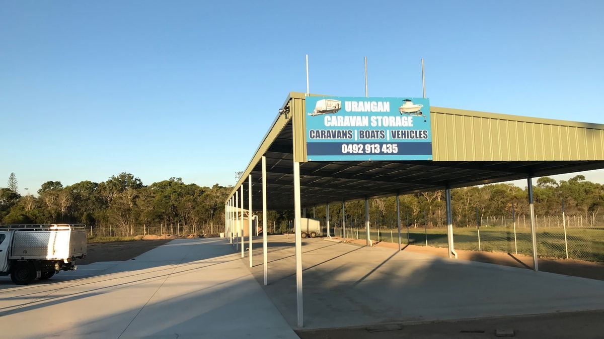 Looking down the row of covered storage bays at Urangan Caravan Storage in late afternoon light, with steel posts and a green Colorbond roof over a pale concrete slab.