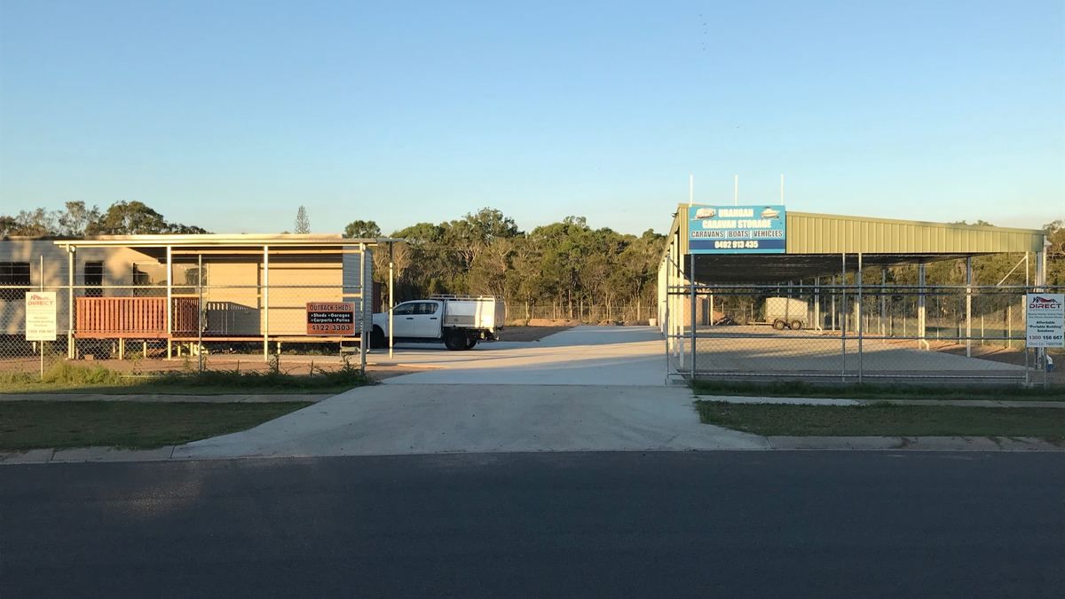 The open gateway to Urangan Caravan Storage on Southern Cross Circuit in late afternoon light, with the green Colorbond shelter and the Urangan Caravan Storage sign behind the mesh fence.